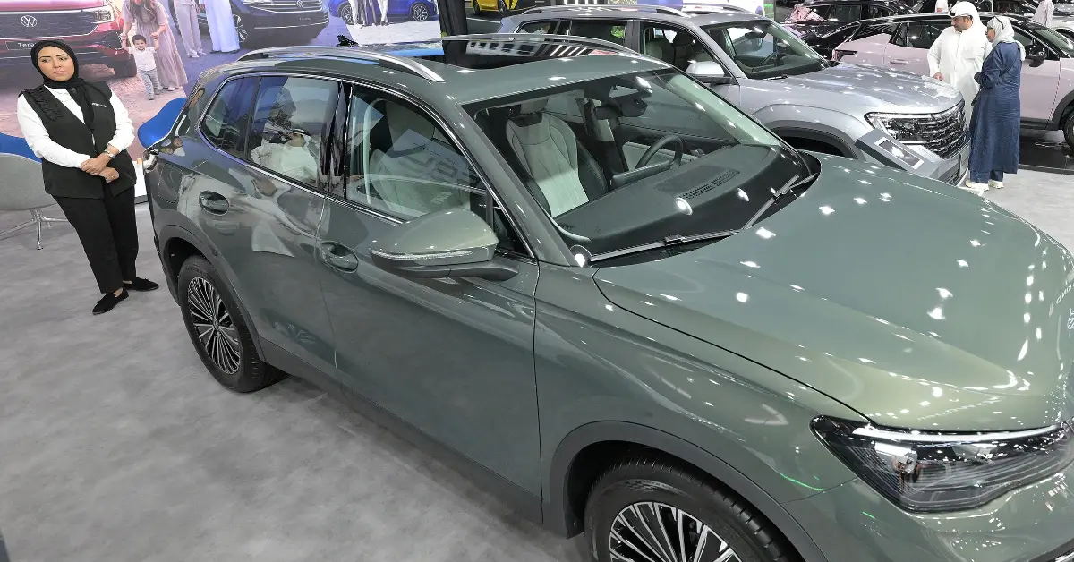 Una mujer vestida de negro y blanco junto a un auto color gris nuevo de la marca volkswagen.jpg