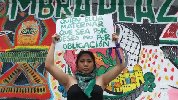 Una mujer joven muestra un cartel con la leyenda "quien elija maternar, que sea por deseo, no por obligación".