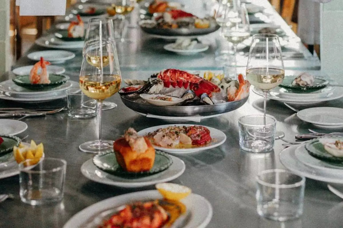 foto de una mesa de restaurante con elegantes platillos como langosta y mariscos y copas de vino blanco
