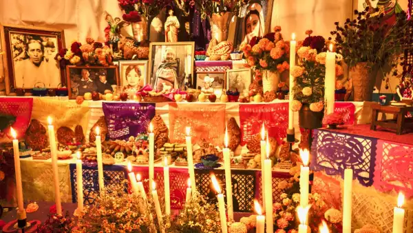 Una ofrenda de día de muertos en la que hay fotos de las personas fallecidas, velas prendidas, papel picado, flores de cempasúchil y alimentos. 