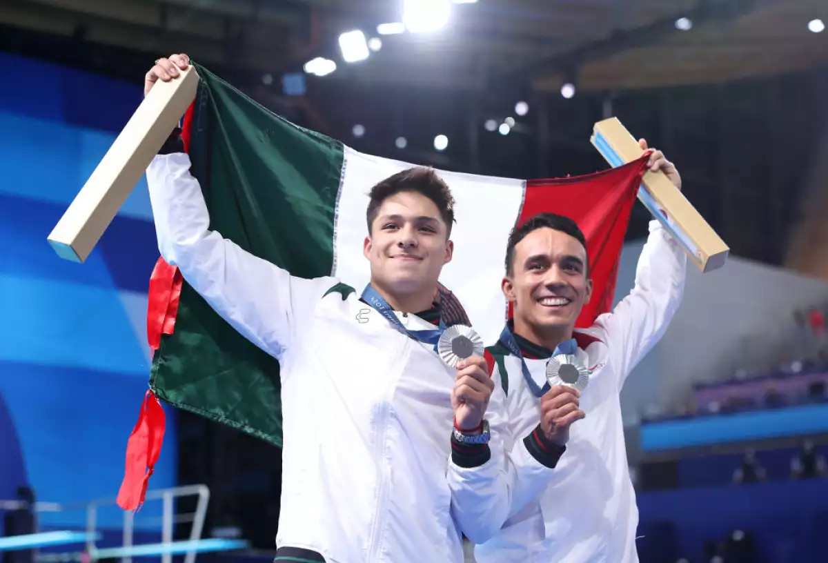 Osmar Olvera y Juan Manuel Celaya sosteniendo la bandera de México con sus medallas de plata en el cuello