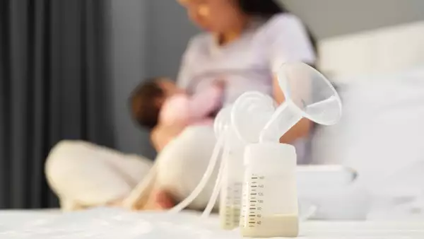 the breast milk are in the bottles of electric breast pumping set on bed with mother breastfeeding newborm baby background