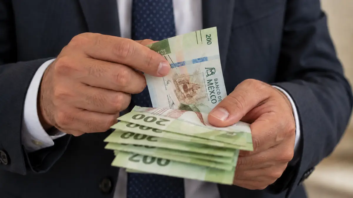 Hombre vestido con traje oscuro contando billetes mexicanos de 200 pesos con ambas manos.