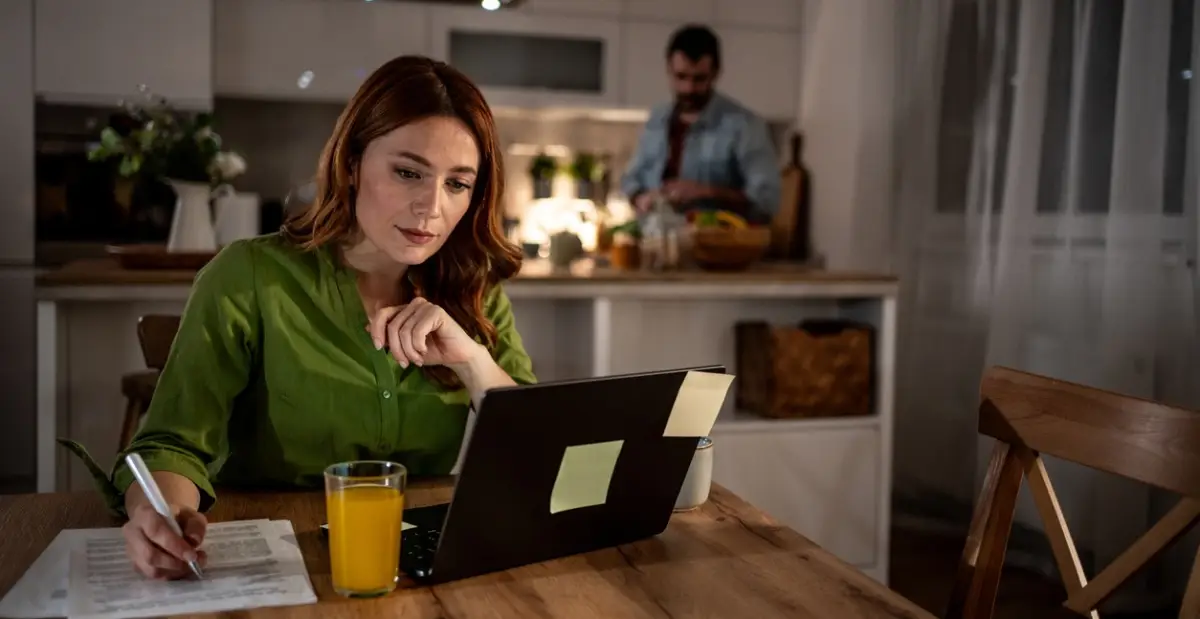 Focused woman working from home while man prepares dinner