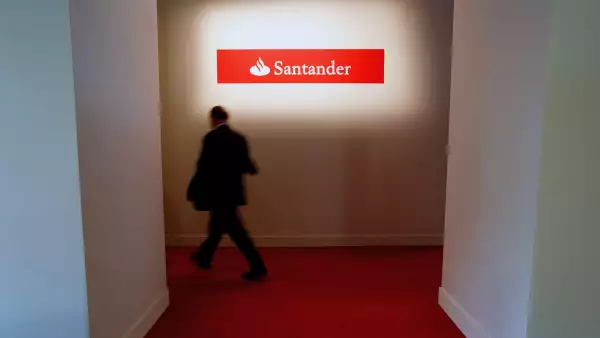 (Un hombre camina frente a un letrero de banco Santander)