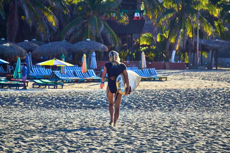 girl walking with a surf board and lounges on the background, zicatela puerto escondido oaxaca