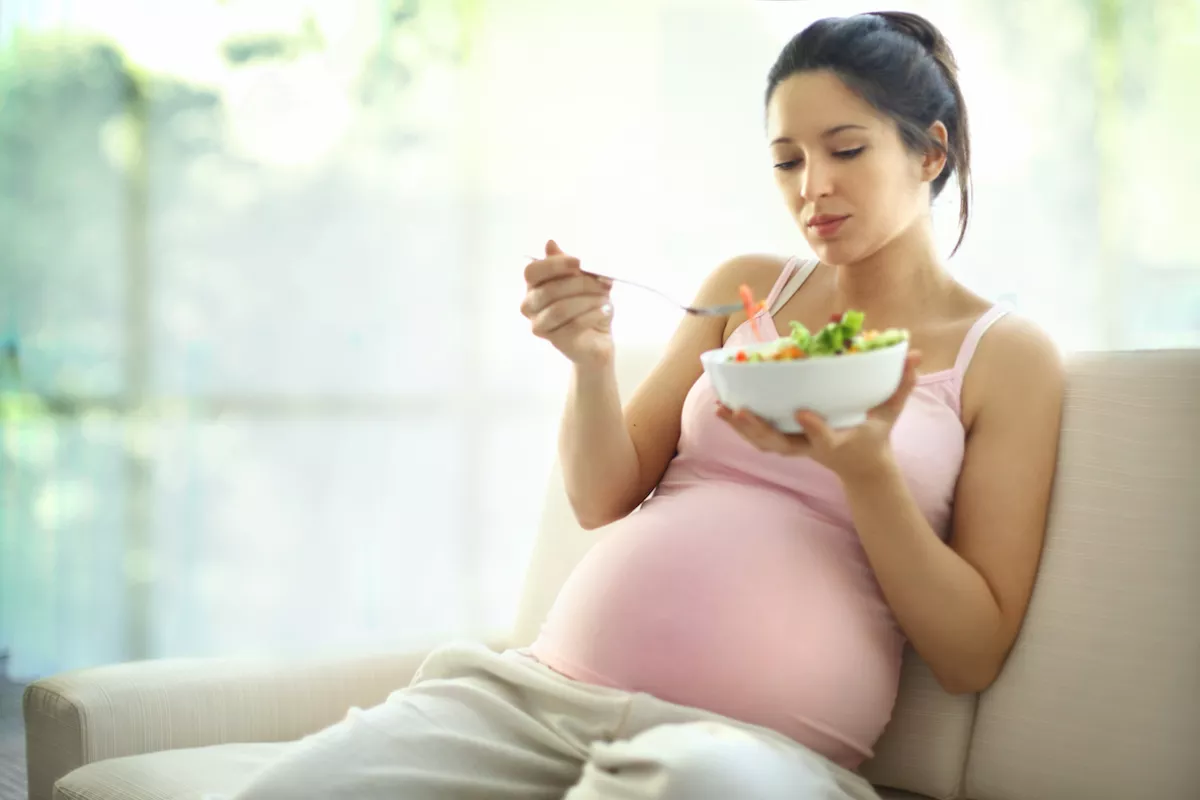 Pregnant woman relaxing at home and eating salad.