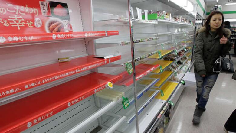 Una mujer busca provisiones en una tienda de Tokio, a pesar de que las tiendas muestran muy poca comida y agua.
