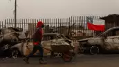 Un residente empuja una carretilla a lo largo de una calle bordeada con los restos carbonizados de vehículos destruidos después de que un incendio forestal devastara Lirquen, una ciudad en Penco cerca de la ciudad de Concepción, Chile, el 20 de enero de 2026. Los bomberos que luchan contra los principales incendios forestales en el sur de Chile que han matado a 20 personas en los últimos cuatro días se beneficiaron del clima más frío a principios del 20 de enero, dijeron las autoridades.