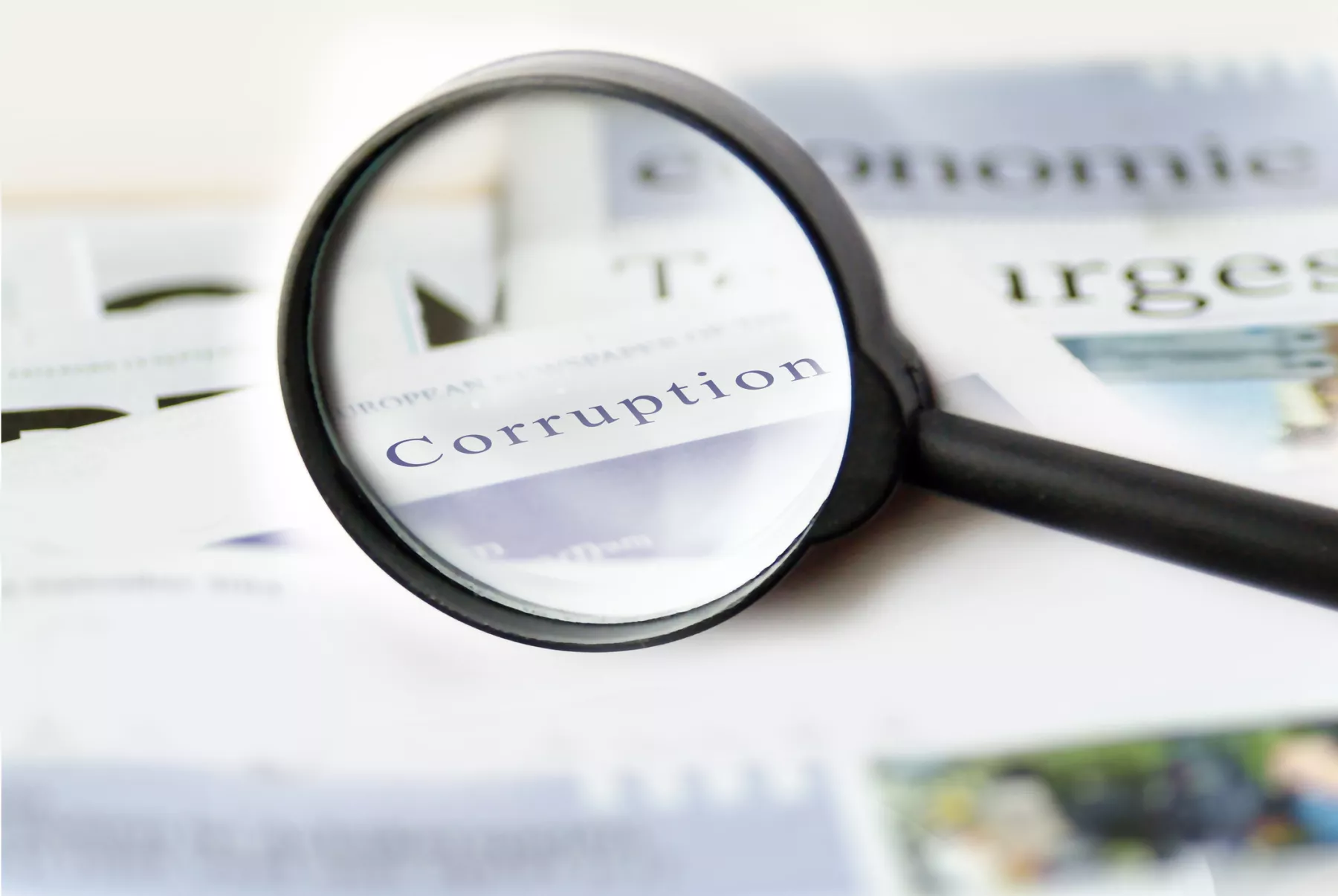 Corruption news concept showing a printed newspaper with a magnifying glass