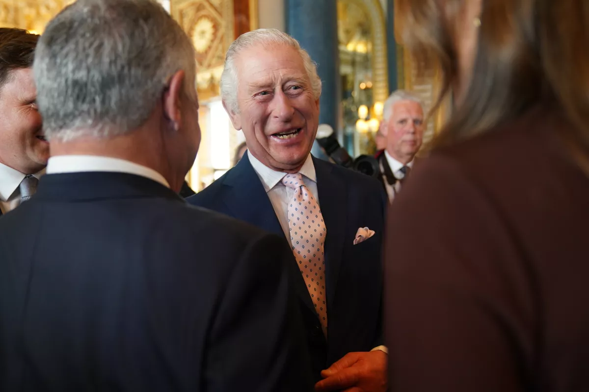 El rey Carlos III sonriente con un traje azul, corbata y pañuelo rosa