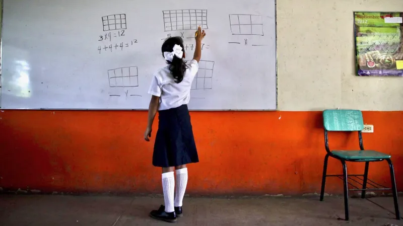 Una alumna de educación básica resuelve un problema matemático frente al pizarrón de un salón de clases.