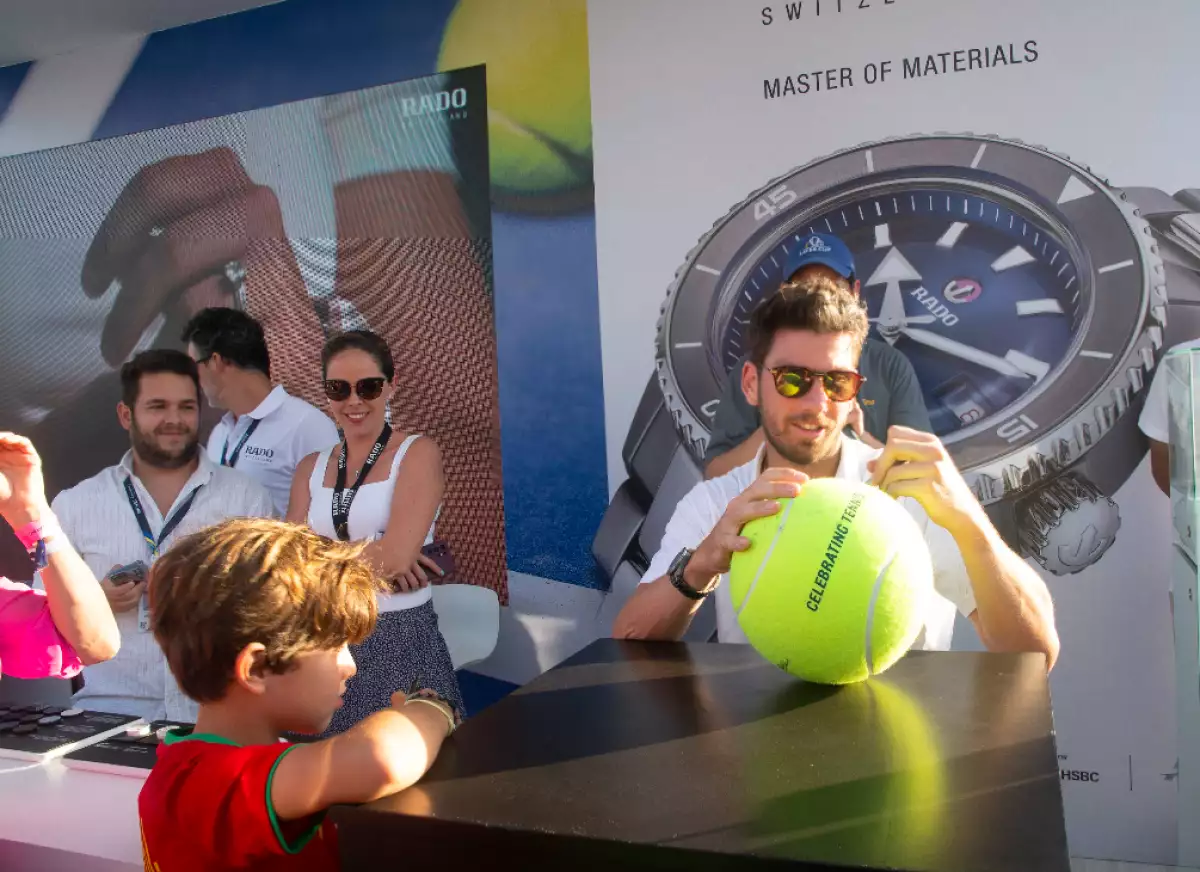 imagen del tenista Cameron Norrie autografiando una pelota de un niño, frente al stand de Rado en el Abierto Mexicano de Tenis 2023.