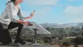 Una mujer tratando de conectar su celular a través de una antena de la empresa Starlink en medio de un cerro. 
