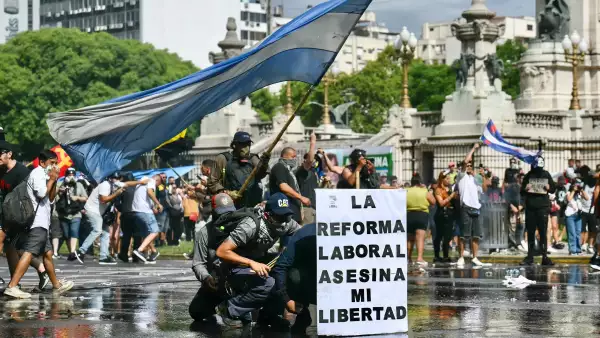 Los manifestantes se protegen detrás de una pancarta que dice "La reforma laboral mata mi libertad" de un cañón de agua disparado por la policía antidisturbios durante una protesta convocada por los sindicalistas contra el debate sobre la reforma laboral que tiene lugar en el Congreso Nacional en Buenos Aires el 11 de febrero de 2026.