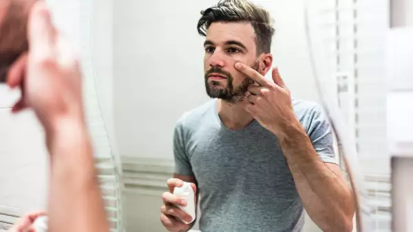 Foto de un hombre frente al espejo tocando su rostro.