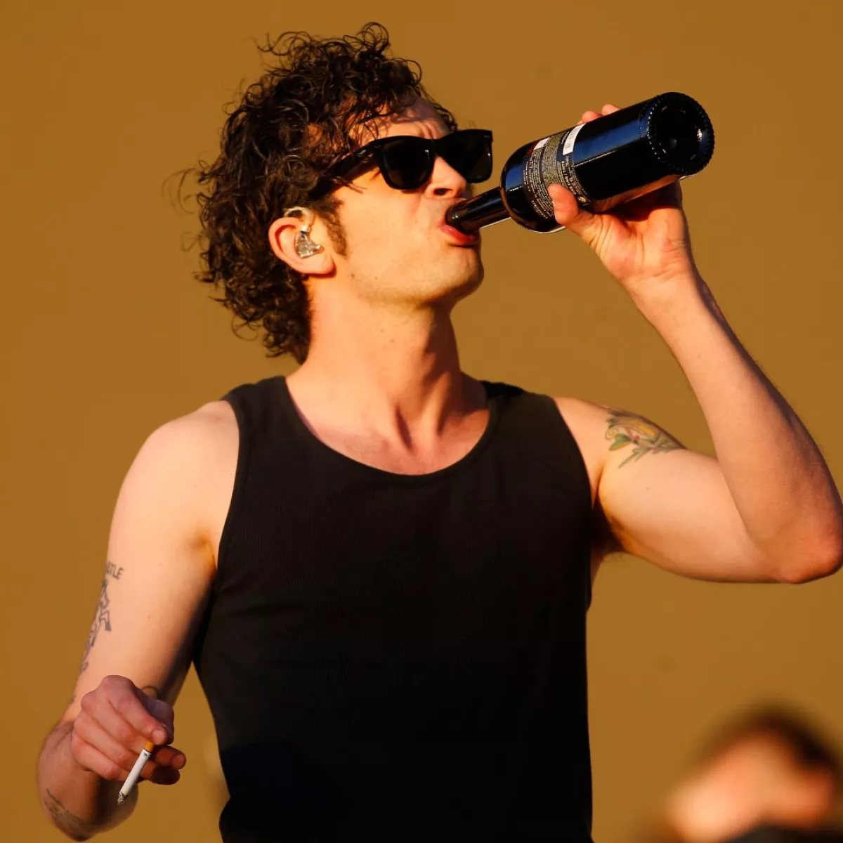 Matty Healy bebe de una botella y sostiene un cigarro