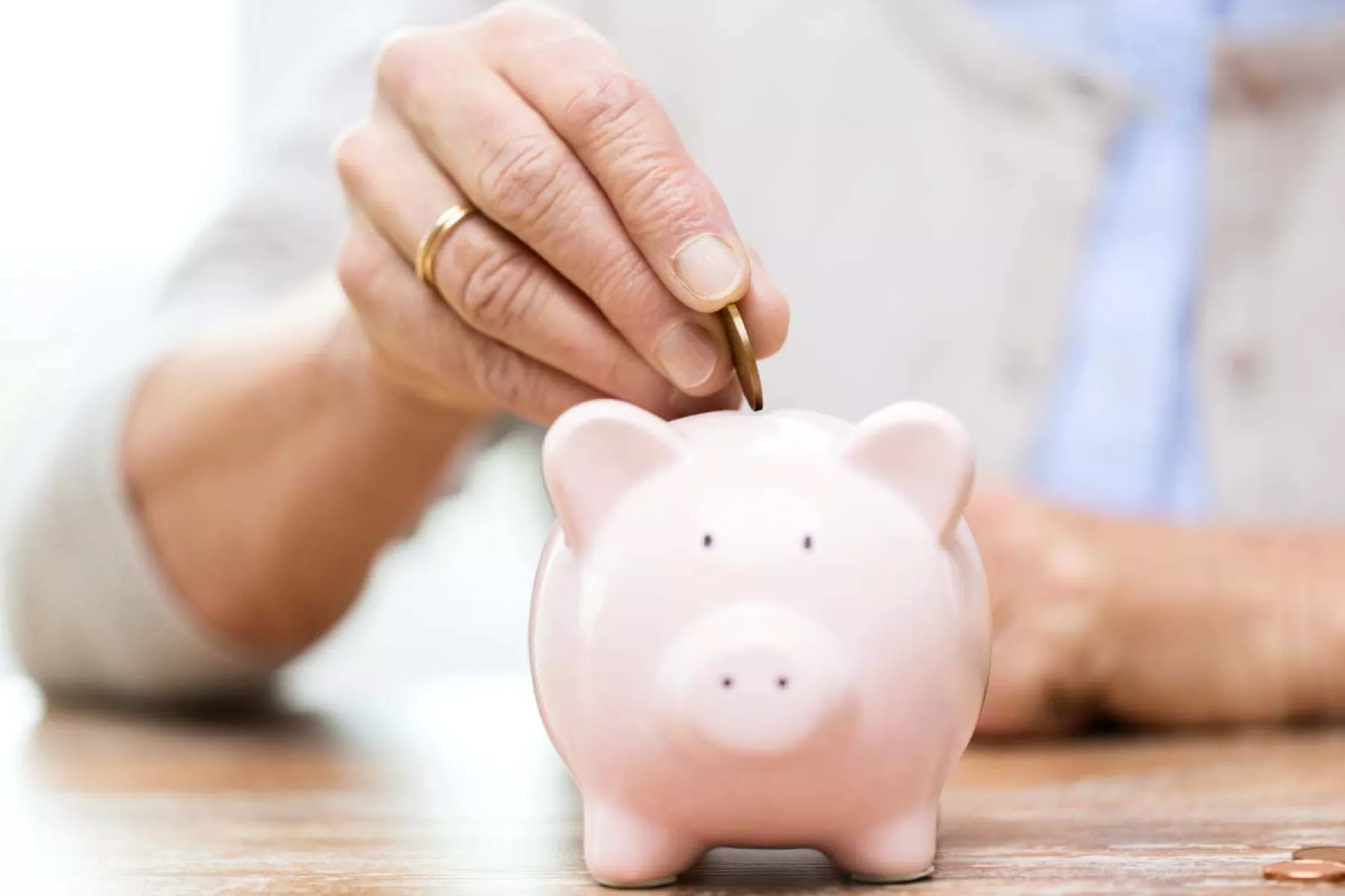 Cómo reclamar la pensión de un trabajador fallecido (La mano de una persona de la tercera edad, metiendo dinero en una alcancía)