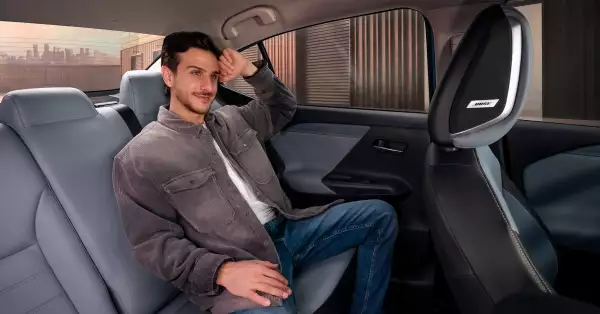 Foto de un joven sentado en las plazas traseras, en donde se aprecia el interior del Nissan Versa 2026 y las bocinas en la cabecera del asiento delantero.