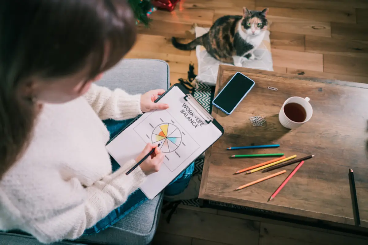 Woman drawing work-life balance wheel sitting on the sofa at home. 