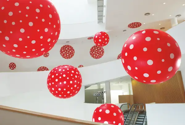 Globos de color rojo con puntos blancos que cuelgan dentro de un inmueble con paredes blancas. 