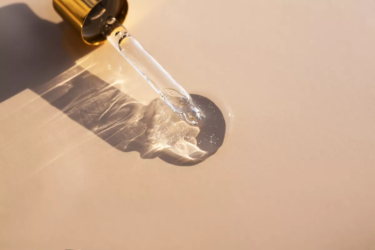 A clear gel-like liquid and a glass pipette casts a shadow on a beige background. Top view, place for text.