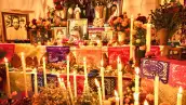 Una ofrenda de día de muertos en la que hay fotos de las personas fallecidas, velas prendidas, papel picado, flores de cempasúchil y alimentos. 