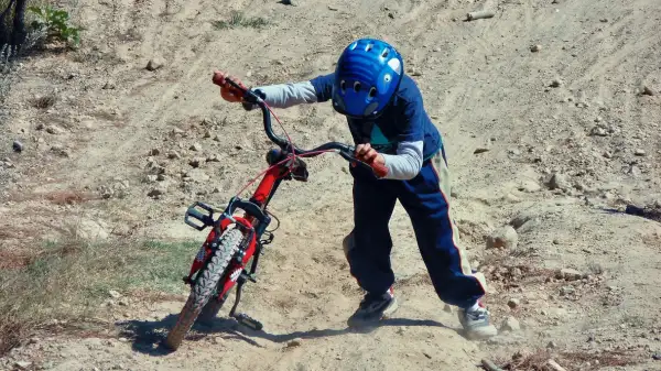 Niño sostiene su bicicleta en un terreno inestable.
