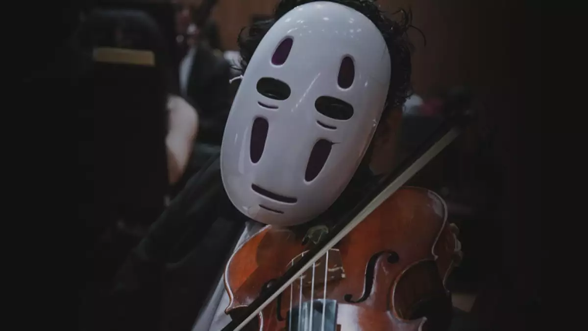 Foto de un hombre tocando la viola con la máscara de "Sin Cara" de la película el Viaje de Chihiro.