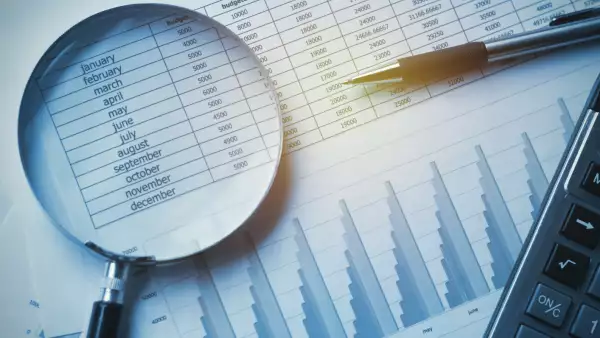 Se observa una hoja con datos numéricos, una calculadora, un lapicero y una lupa.
