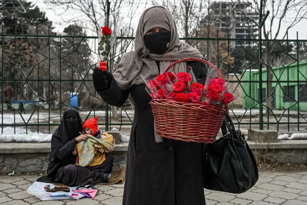 Una mujer afgana carga una canasta llena de rosas para vender, mientras otra mujer trabaja con un chico en una calle de Kabul. 