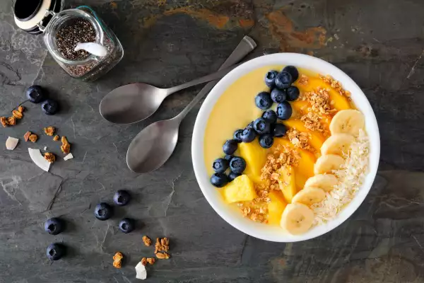 Pineapple, mango smoothie bowl with coconut, bananas, blueberries and granola, above view table scene on slate