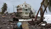 En la imagen se observa una vivienda destruida por el paso del huracán Simón en Colima, así como palmeras dañadas y basura arrastrada a la orilla del mar.