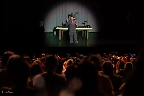 Foto del teatro del centro cultural helénico lleno de personas y al fondo en el escenario se ve a la actriz regina blandón en su papel en la obra Prima Facie