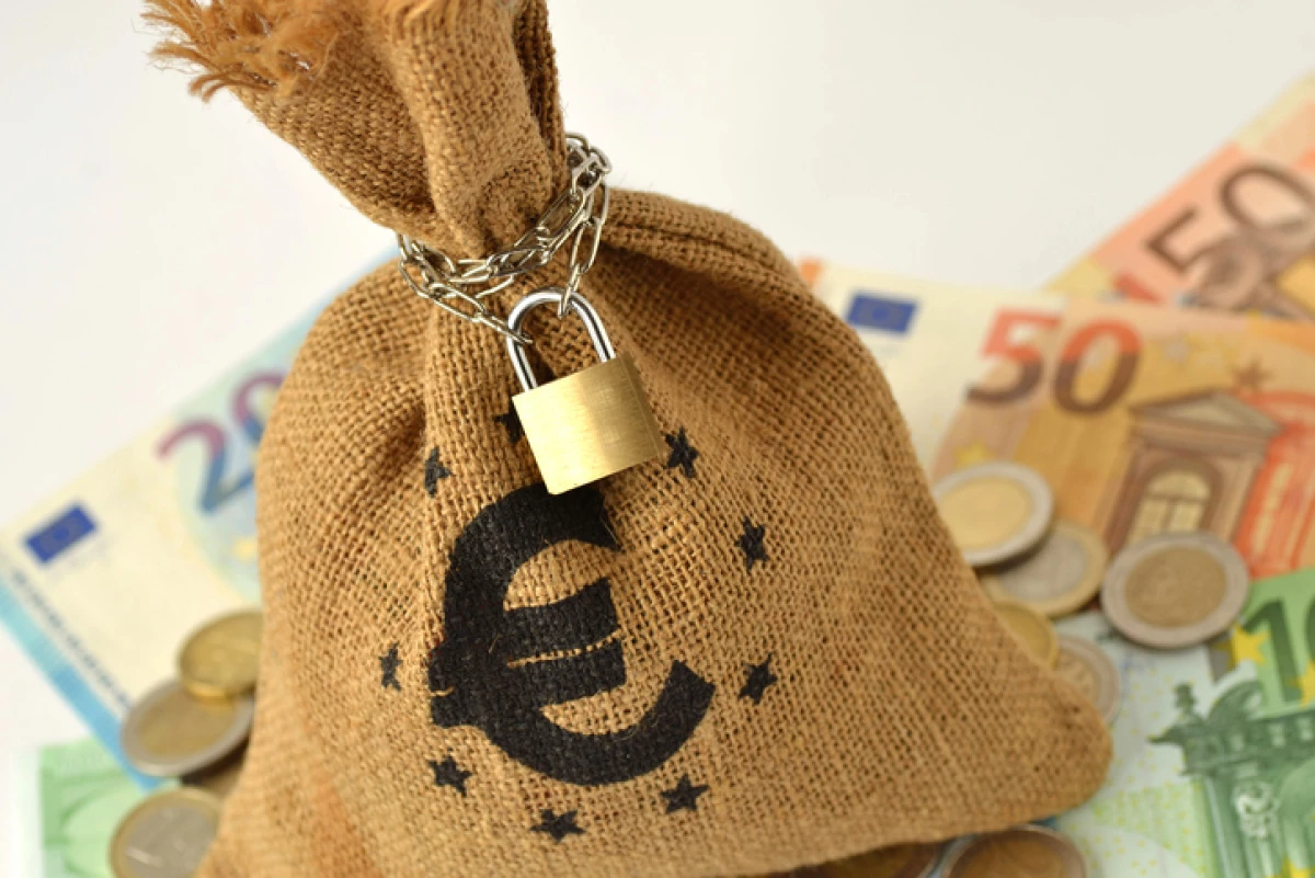 Money bag with padlock and chain over euro banknotes and coins - Saving money and financial security concept
