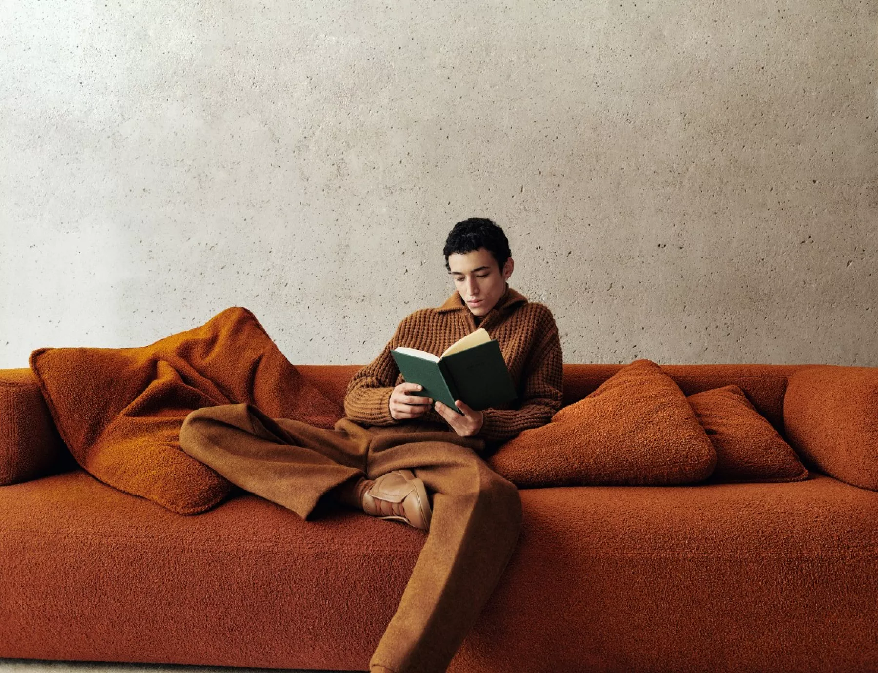 Modelo está sentado en un sillón leyendo, él está vestido en color anaranjado, toda su ropa de la colección Fall Winter 2023 Oasi Cashmere de Zegna.