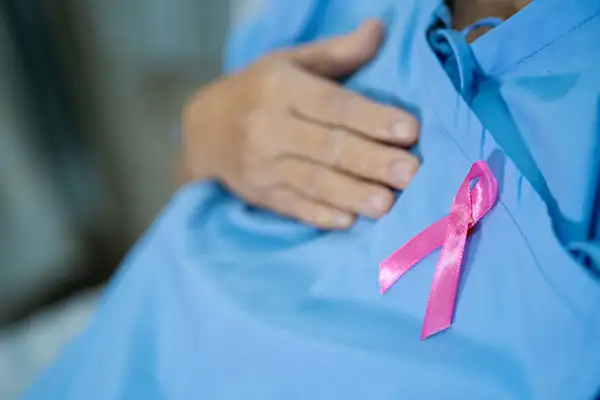 Una mano se recarga sobre una bata azul y sobre el seno derecho donde también hay un moño rosa .jpg