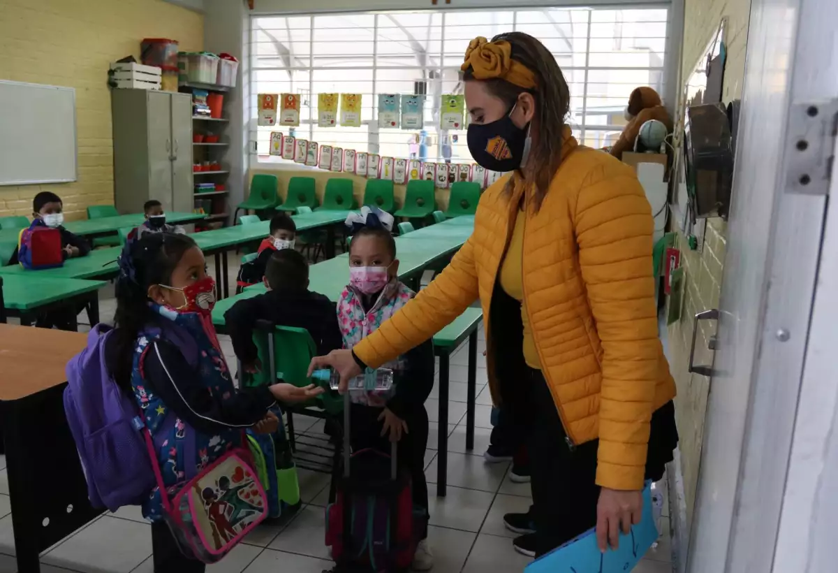 Profesora pone gel antibacterial a una alumna.