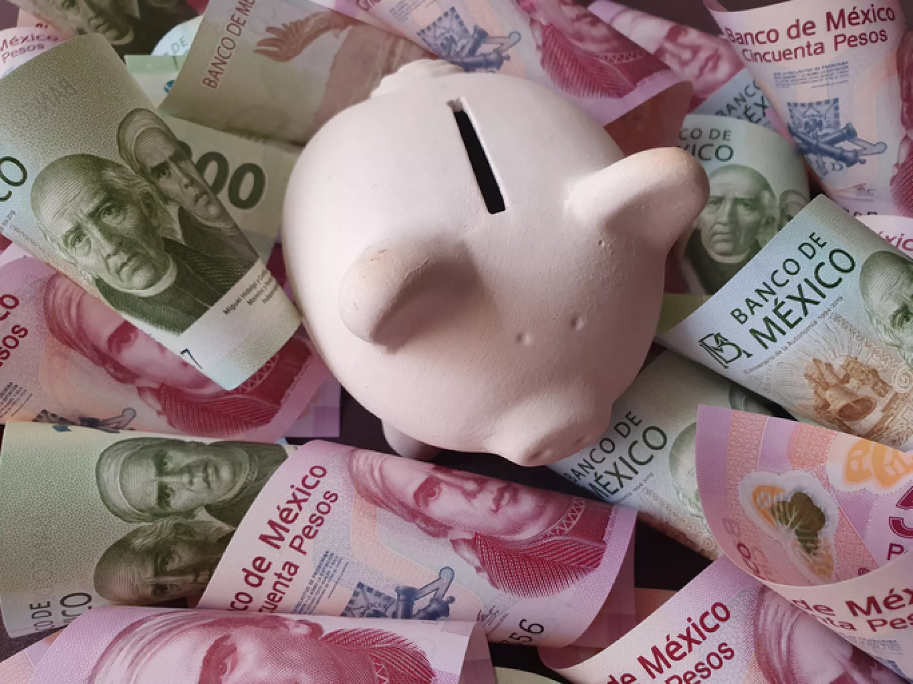 white piggy bank and Mexican banknotes of different denominations