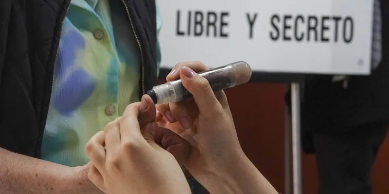 Funcionario de casilla aplica tinta electoral en el pulgar de un votante