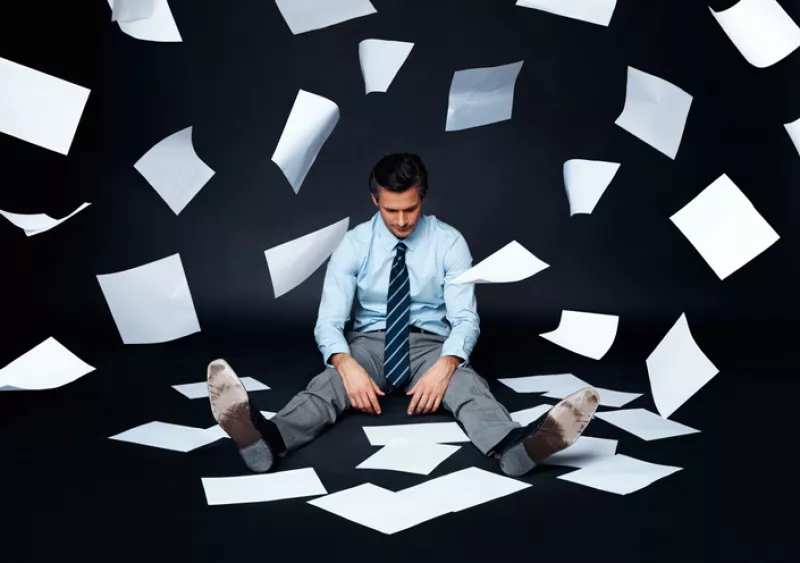 Businessman sitting on a dark surface with papers flying
