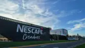 Planta de Nescafé Creadores de Nestlé en Veracruz, con la fachada negra que exhibe el nombre de la marca y edificios industriales al fondo, rodeados de áreas verdes y una vialidad.