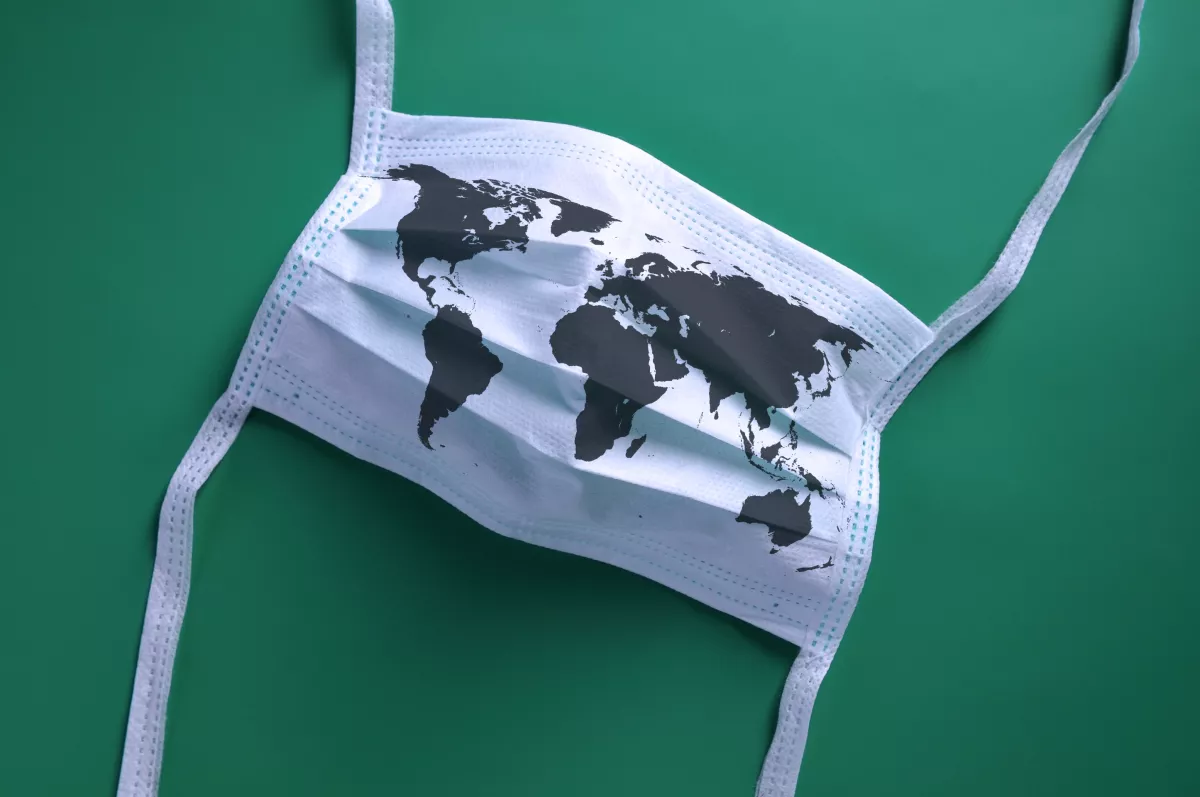 White face mask with a map of the world is lying on a green background