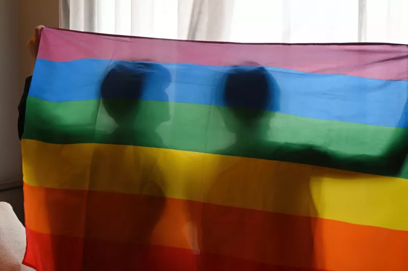 Detrás de la vista y la silueta de la joven pareja gay Pride con las manos levantadas y la bandera LGBT, LGBT, orgullo, relaciones y concepto de igualdad