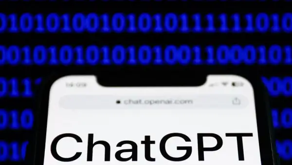 El sitio web de ChatGPT se muestra en la pantalla de un teléfono y un código binario se muestra en una pantalla de fondo.