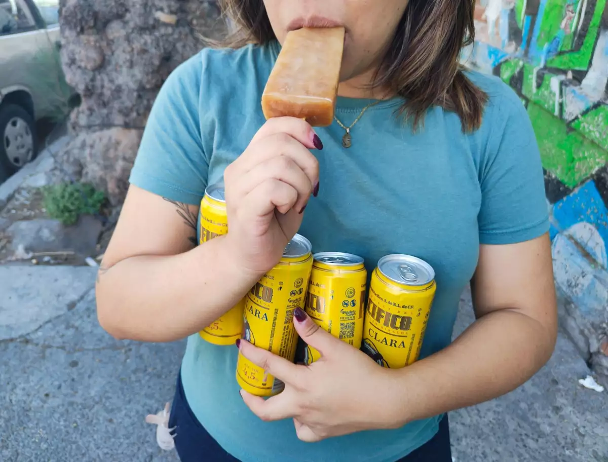 Una persona lleva consigo unas latas de cerveza mientras come una paleta de hielo.