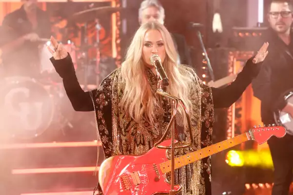 Foto de la cantante Carrie Underwood cantando en un escenario con una guitarra roja.