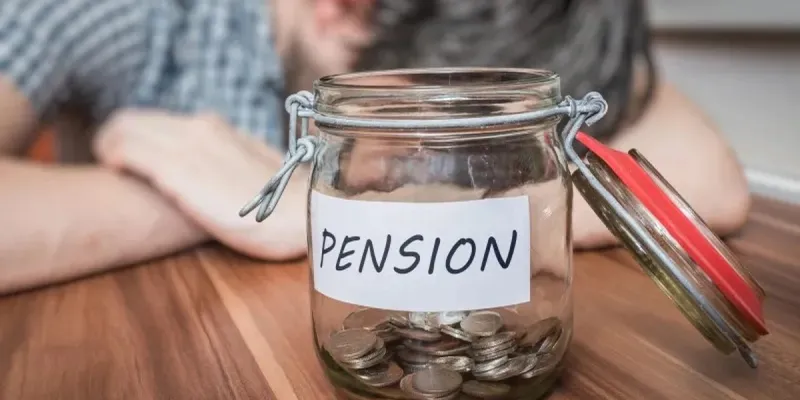 Persona recostada sobre una mesa y un tarro de vidrio con monedas y el emblema pensión.