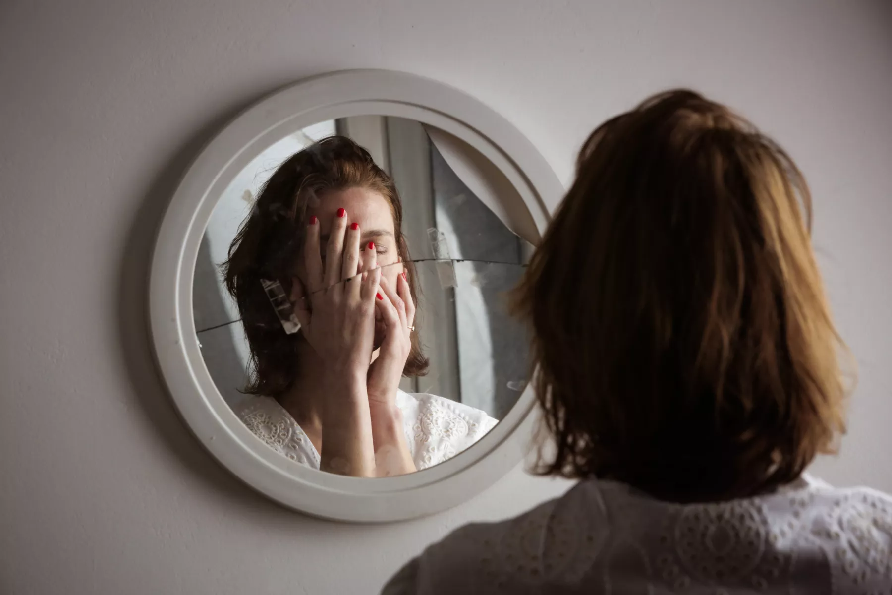 El trastorno bipolar tiene varios síntomas. (Mujer frente a un espejo tapándose la cara)