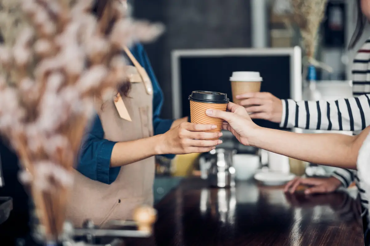 Barista entregando café en vaso para llevar al comensal